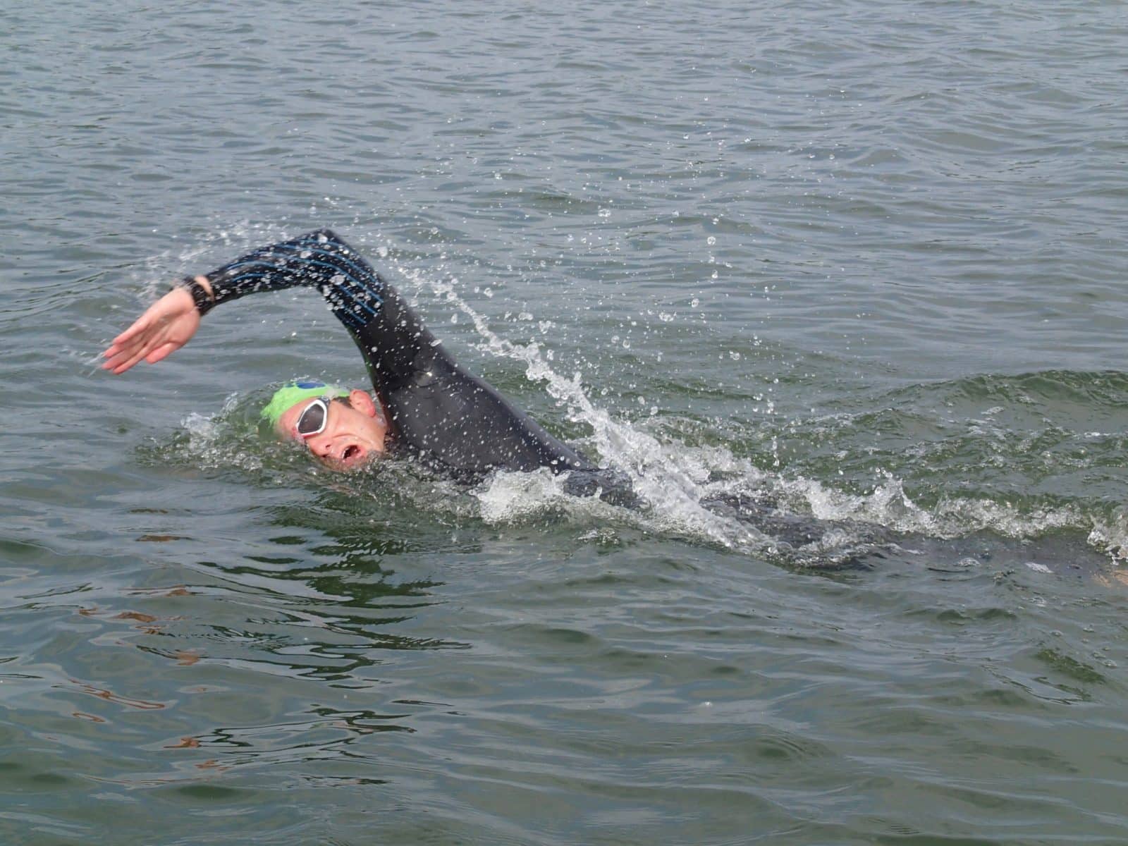 Triathlete open water swimming in lake on a summer’s day. Man wearing goggles practicing swim stroke. sport, action, motion and movement